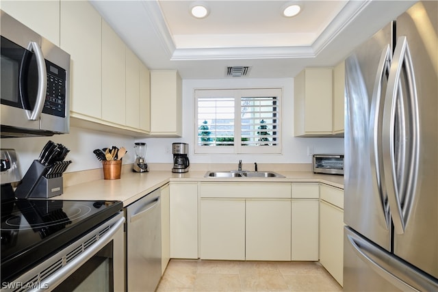 kitchen featuring appliances with stainless steel finishes, a raised ceiling, sink, light tile patterned floors, and cream cabinetry