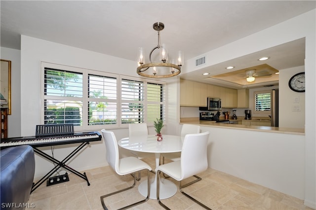 dining space featuring a raised ceiling, a wealth of natural light, sink, and ceiling fan with notable chandelier