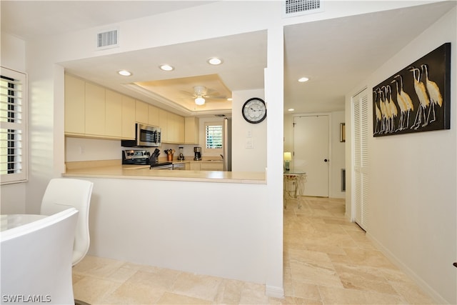 kitchen with ceiling fan, a raised ceiling, kitchen peninsula, and appliances with stainless steel finishes