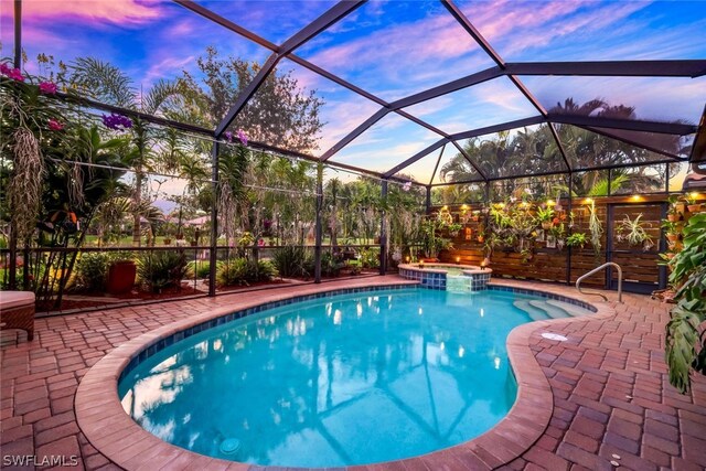 pool at dusk with a lanai, an in ground hot tub, and a patio