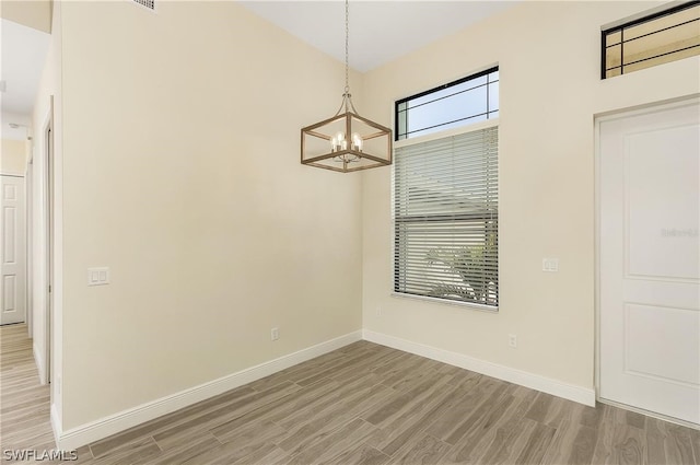 spare room featuring a chandelier and light wood-type flooring