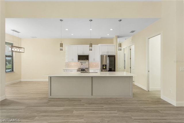 kitchen with pendant lighting, stainless steel appliances, white cabinetry, and a kitchen island with sink