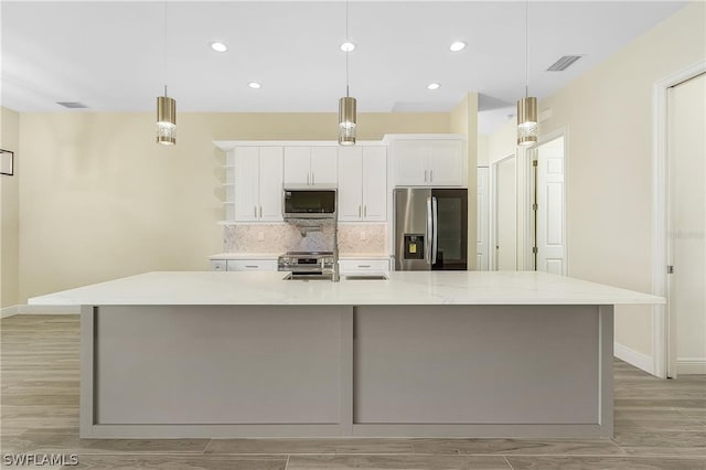 kitchen with pendant lighting, an island with sink, stainless steel appliances, and white cabinets