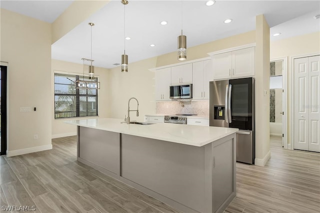 kitchen featuring decorative light fixtures, a kitchen island with sink, appliances with stainless steel finishes, light hardwood / wood-style flooring, and white cabinets