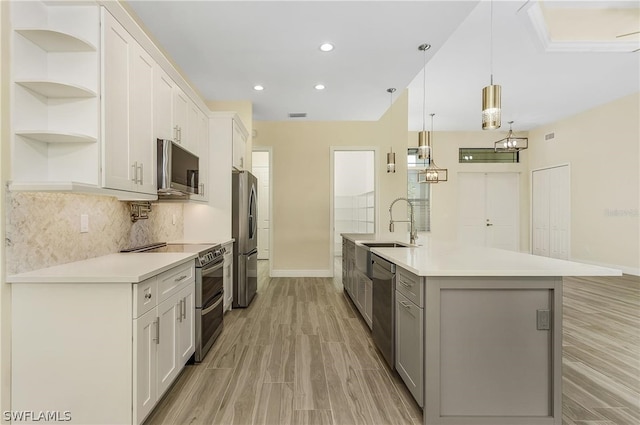 kitchen featuring a kitchen island with sink, appliances with stainless steel finishes, tasteful backsplash, white cabinetry, and light wood-type flooring