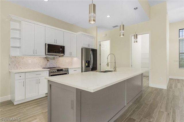 kitchen featuring appliances with stainless steel finishes, decorative light fixtures, an island with sink, and white cabinetry