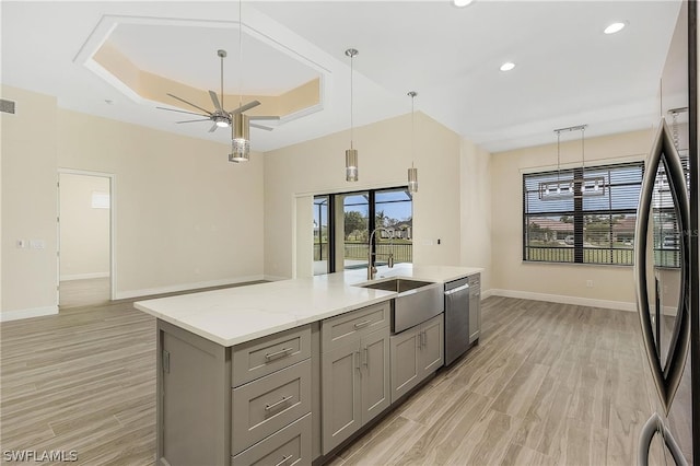 kitchen featuring decorative light fixtures, ceiling fan, a center island with sink, light hardwood / wood-style flooring, and a raised ceiling