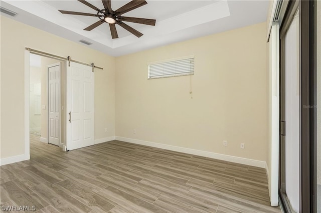 unfurnished room featuring a barn door, ceiling fan, a tray ceiling, and light hardwood / wood-style flooring