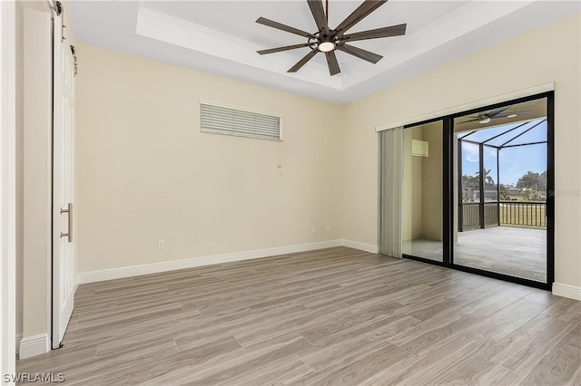 unfurnished room featuring a barn door, ceiling fan, a tray ceiling, and light hardwood / wood-style flooring