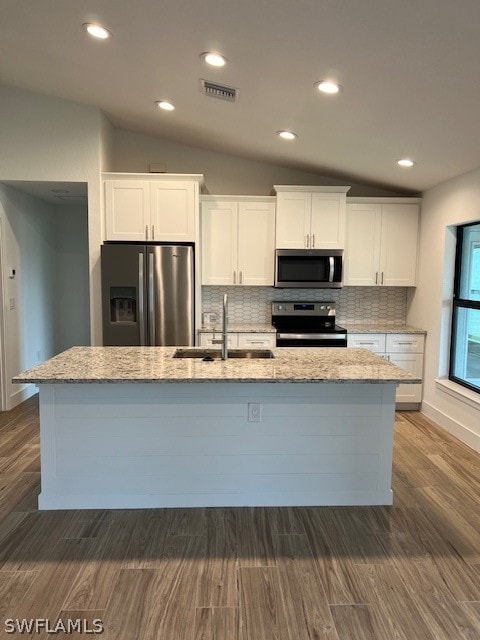 kitchen with backsplash, stainless steel appliances, lofted ceiling, an island with sink, and white cabinetry