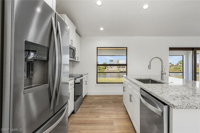 kitchen featuring white cabinets, light wood-type flooring, light stone countertops, stainless steel appliances, and sink