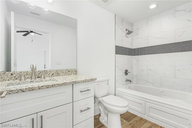 full bathroom featuring ceiling fan, tiled shower / bath, vanity with extensive cabinet space, hardwood / wood-style floors, and toilet