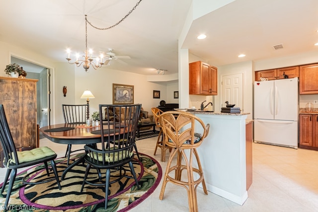 kitchen with ceiling fan with notable chandelier, white fridge, light stone counters, and kitchen peninsula