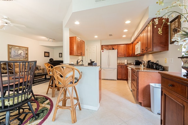 kitchen with kitchen peninsula, ceiling fan, light stone counters, and white appliances