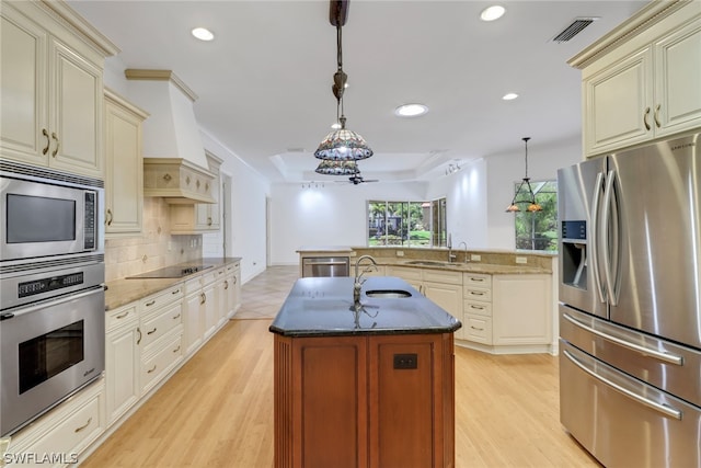 kitchen with hanging light fixtures, light wood-type flooring, an island with sink, stainless steel appliances, and sink