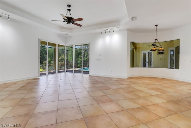 empty room with ceiling fan, track lighting, a tray ceiling, and light tile floors