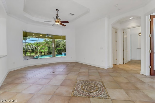 tiled empty room with ceiling fan and a tray ceiling