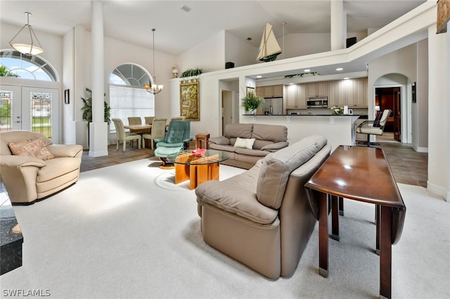 carpeted living room featuring an inviting chandelier, high vaulted ceiling, and french doors