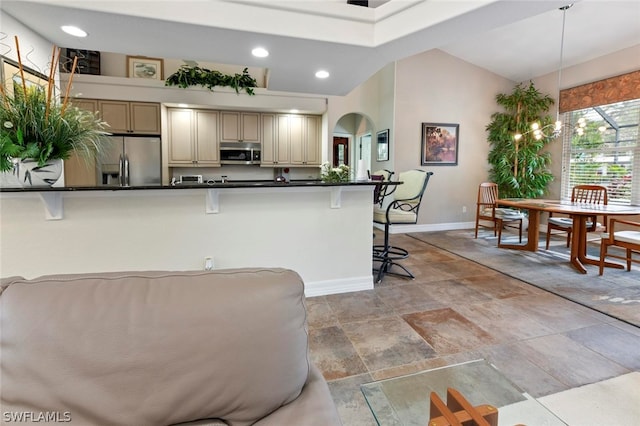 kitchen with appliances with stainless steel finishes, cream cabinetry, vaulted ceiling, light tile floors, and a kitchen breakfast bar