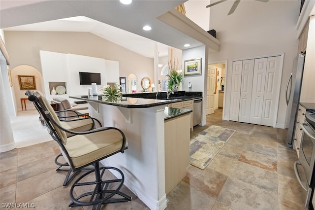 kitchen featuring stainless steel appliances, light tile floors, a kitchen breakfast bar, dark stone counters, and ceiling fan