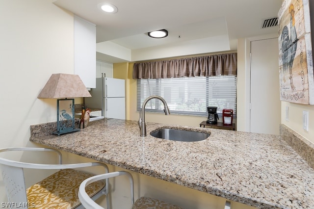 kitchen with light stone counters, white fridge, kitchen peninsula, and sink