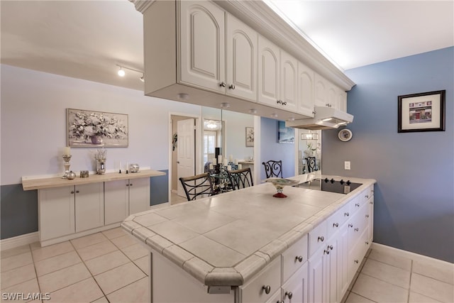 kitchen featuring tile counters, kitchen peninsula, light tile floors, white cabinets, and black electric cooktop