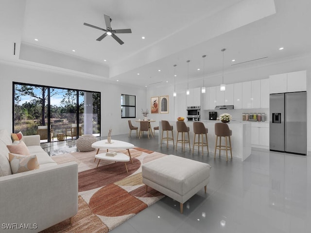 tiled living room with a raised ceiling and ceiling fan