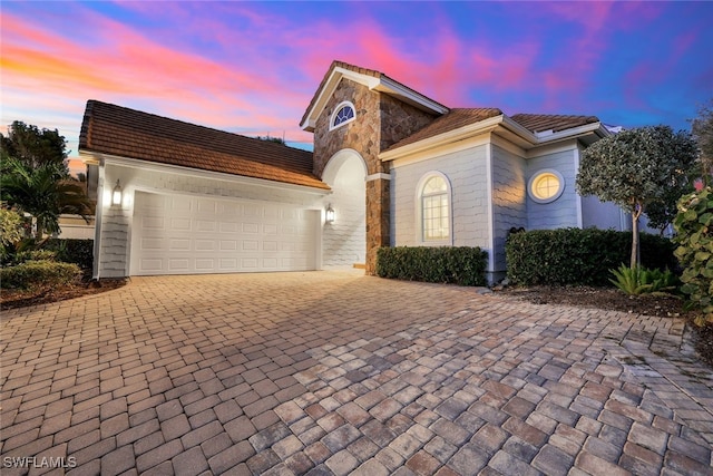 mediterranean / spanish house with stone siding, decorative driveway, and an attached garage