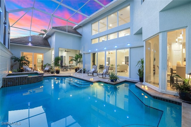 pool at dusk featuring a patio area, a lanai, and a pool with connected hot tub