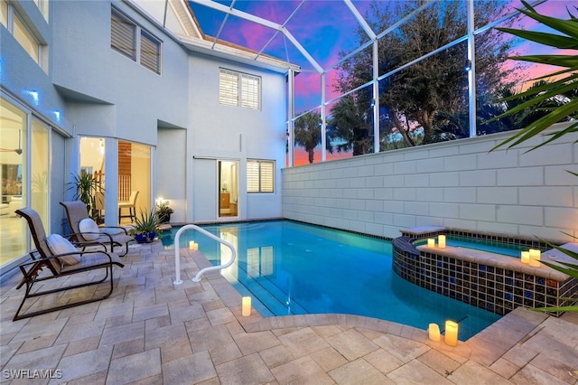 pool at dusk with a patio area, a pool with connected hot tub, and glass enclosure