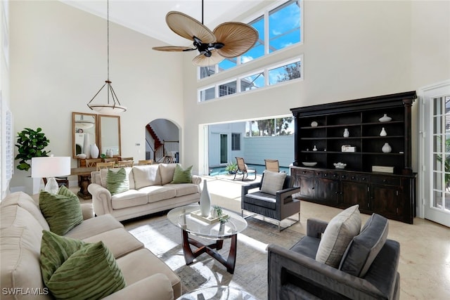 living room featuring arched walkways, ceiling fan, stairway, and a towering ceiling