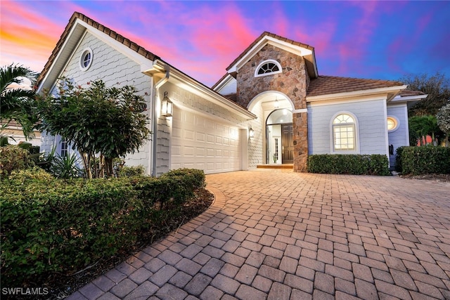 view of front of property featuring stone siding, decorative driveway, and an attached garage