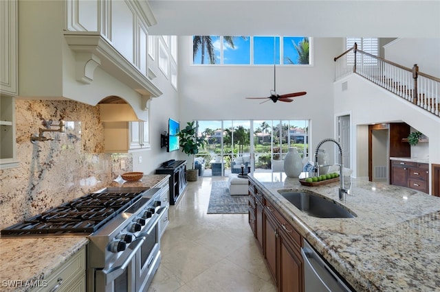 kitchen with light stone counters, stainless steel appliances, a sink, a ceiling fan, and tasteful backsplash