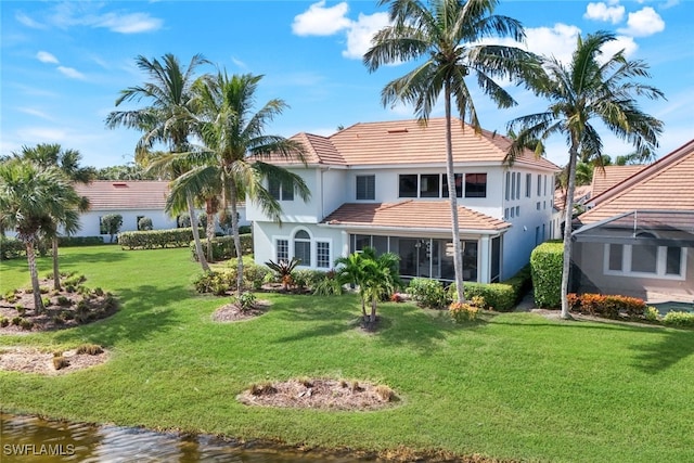 rear view of house with a lawn, a water view, a tile roof, and a sunroom