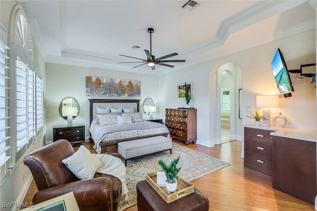 bedroom with arched walkways, a raised ceiling, visible vents, and multiple windows