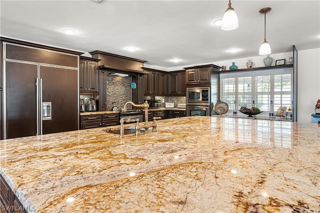 kitchen with pendant lighting, built in appliances, tasteful backsplash, dark brown cabinetry, and sink