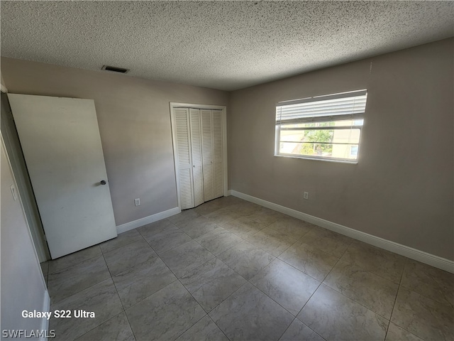 unfurnished bedroom with light tile flooring, a textured ceiling, and a closet