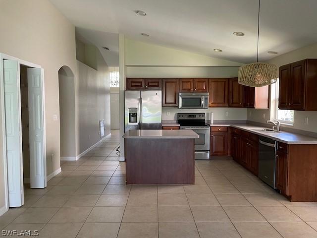 kitchen with a center island, stainless steel appliances, vaulted ceiling, decorative light fixtures, and light tile patterned floors