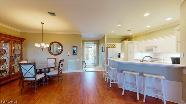 kitchen with hardwood / wood-style flooring, hanging light fixtures, ornamental molding, white cabinetry, and white appliances