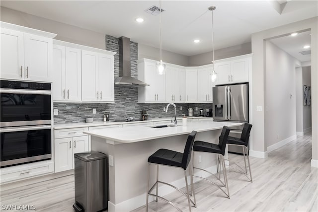 kitchen with wall chimney exhaust hood, light wood-type flooring, backsplash, stainless steel appliances, and sink