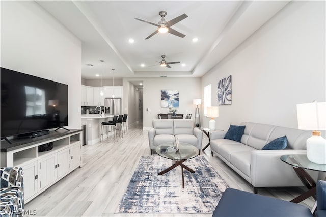 living room with baseboards, recessed lighting, a ceiling fan, light wood-style floors, and a raised ceiling