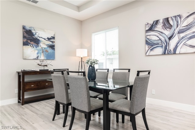 dining area featuring a tray ceiling, light wood-type flooring, and baseboards