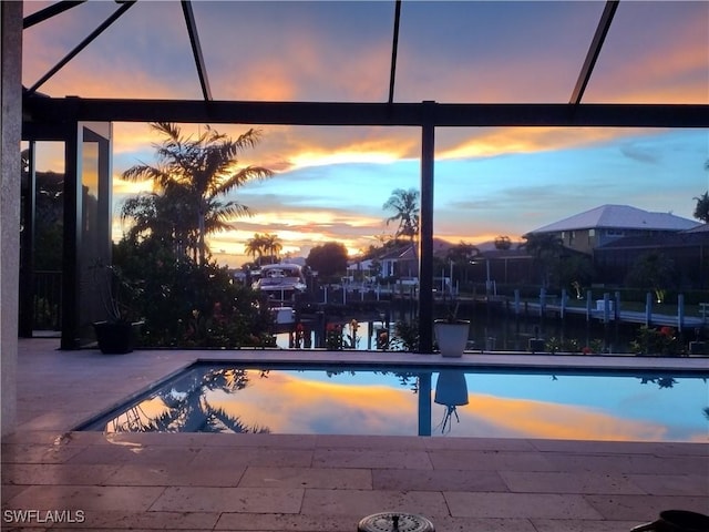 pool at dusk with glass enclosure, a water view, and a patio