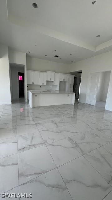 unfurnished living room with light tile flooring and a raised ceiling