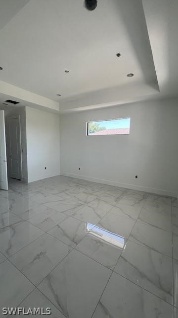 empty room with a raised ceiling and light tile floors