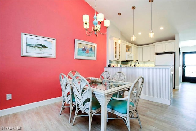 dining room featuring an inviting chandelier, lofted ceiling, sink, and light hardwood / wood-style flooring