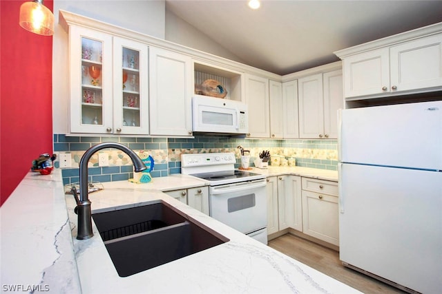 kitchen with light stone countertops, backsplash, white appliances, sink, and vaulted ceiling