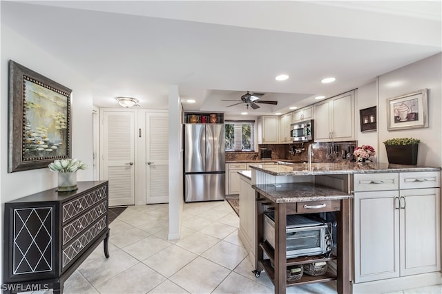 kitchen featuring tasteful backsplash, ceiling fan, stainless steel appliances, dark stone countertops, and light tile floors