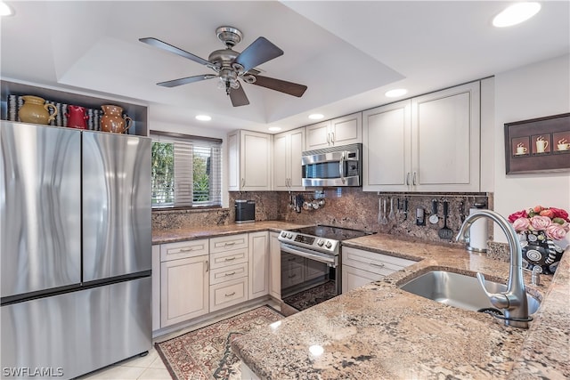 kitchen featuring backsplash, appliances with stainless steel finishes, sink, ceiling fan, and light stone counters