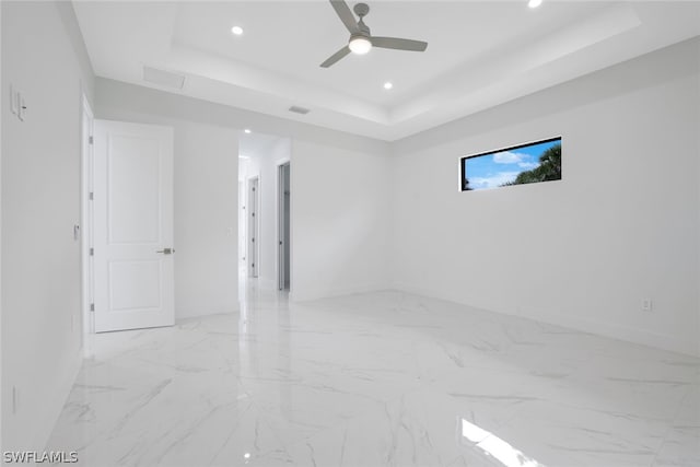 tiled empty room featuring ceiling fan and a raised ceiling